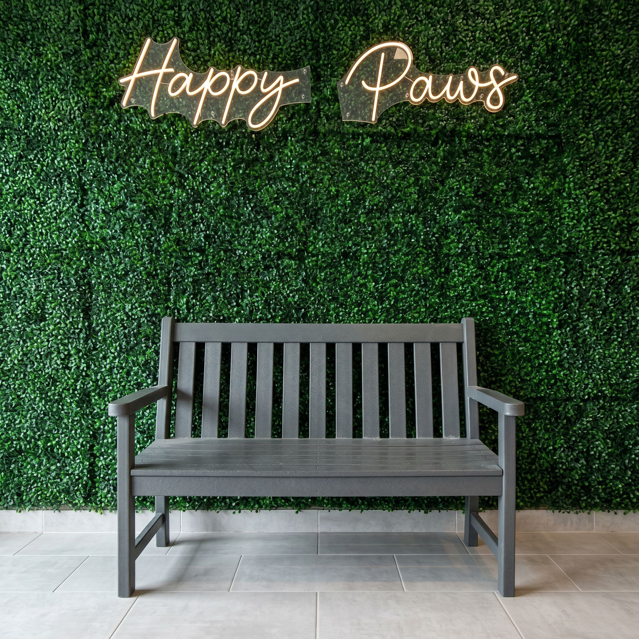 The Happy Paws wall: green hedge with the lit neon sign above a grey bench